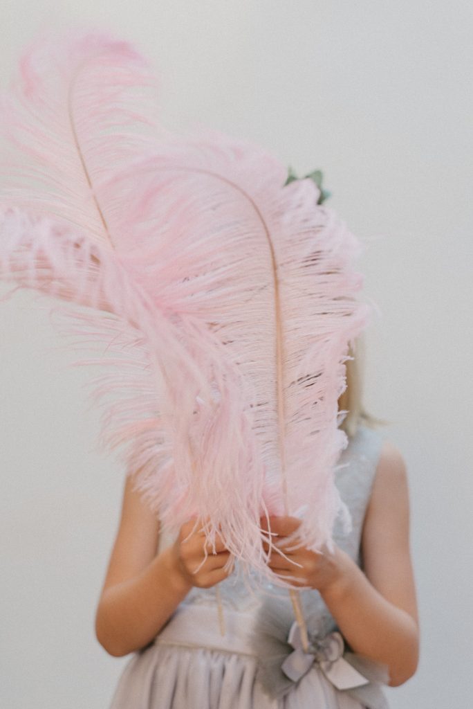 Ein Mädchen versteckt sich hinter rosa Federn - Symbolbild zum Text über Hochsensibilität